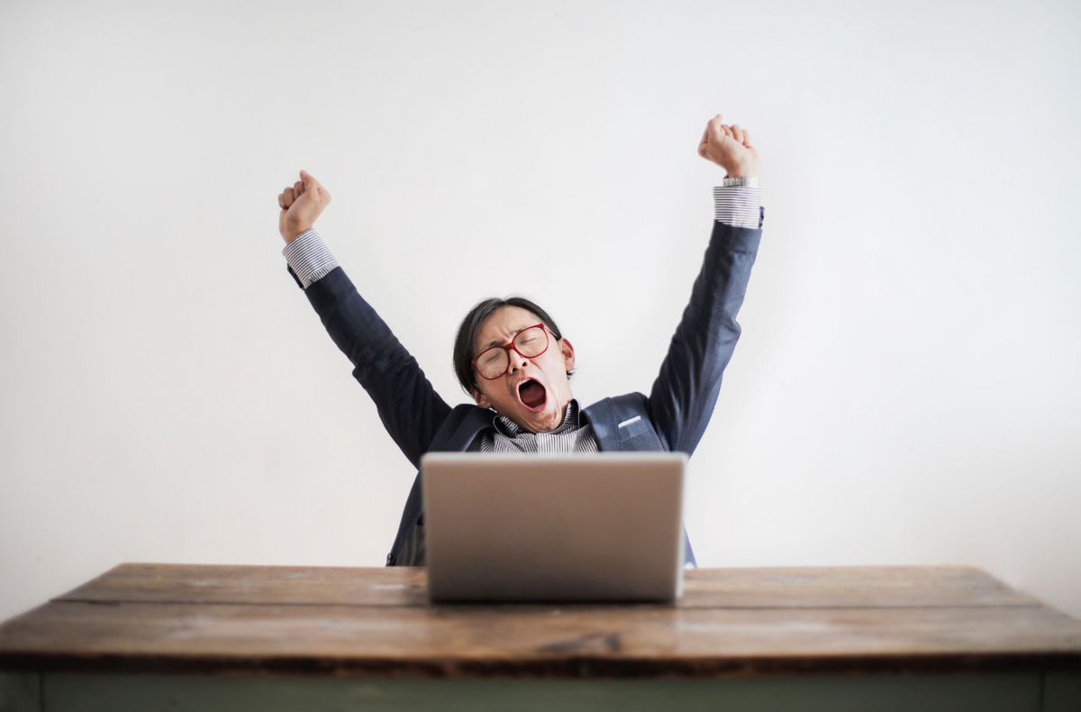 A person is sitting at a desk while yawning and stretching their arms.