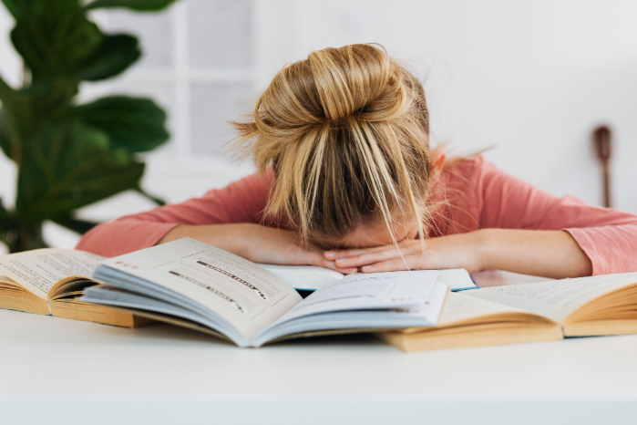 A person with blond hair in a bun rests their head on open books.
