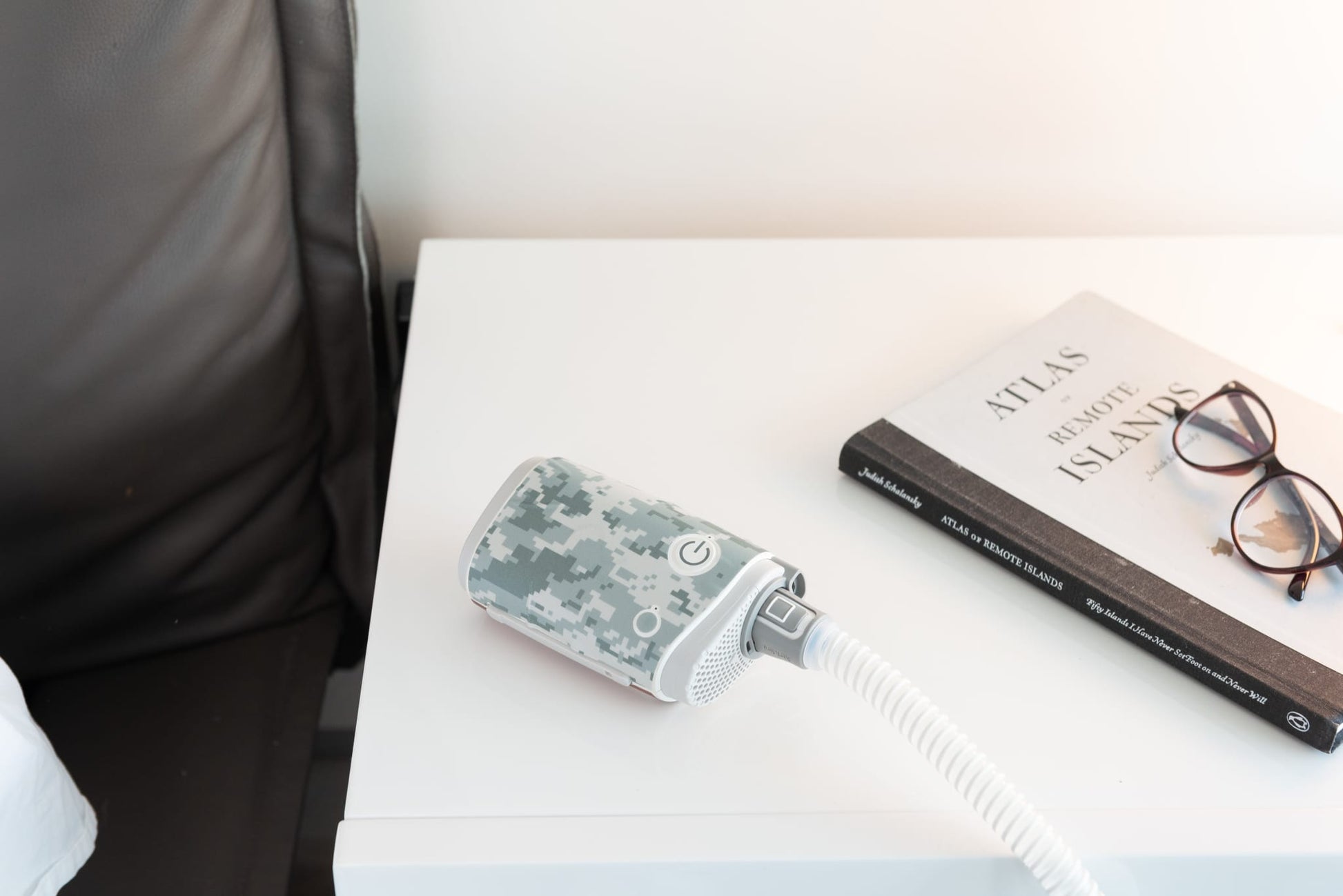 Digital camo Snugell skin on AirMini Travel CPAP Machine with a book and glasses on bedside table, ideal for users seeking a rugged look for their CPAP equipment."