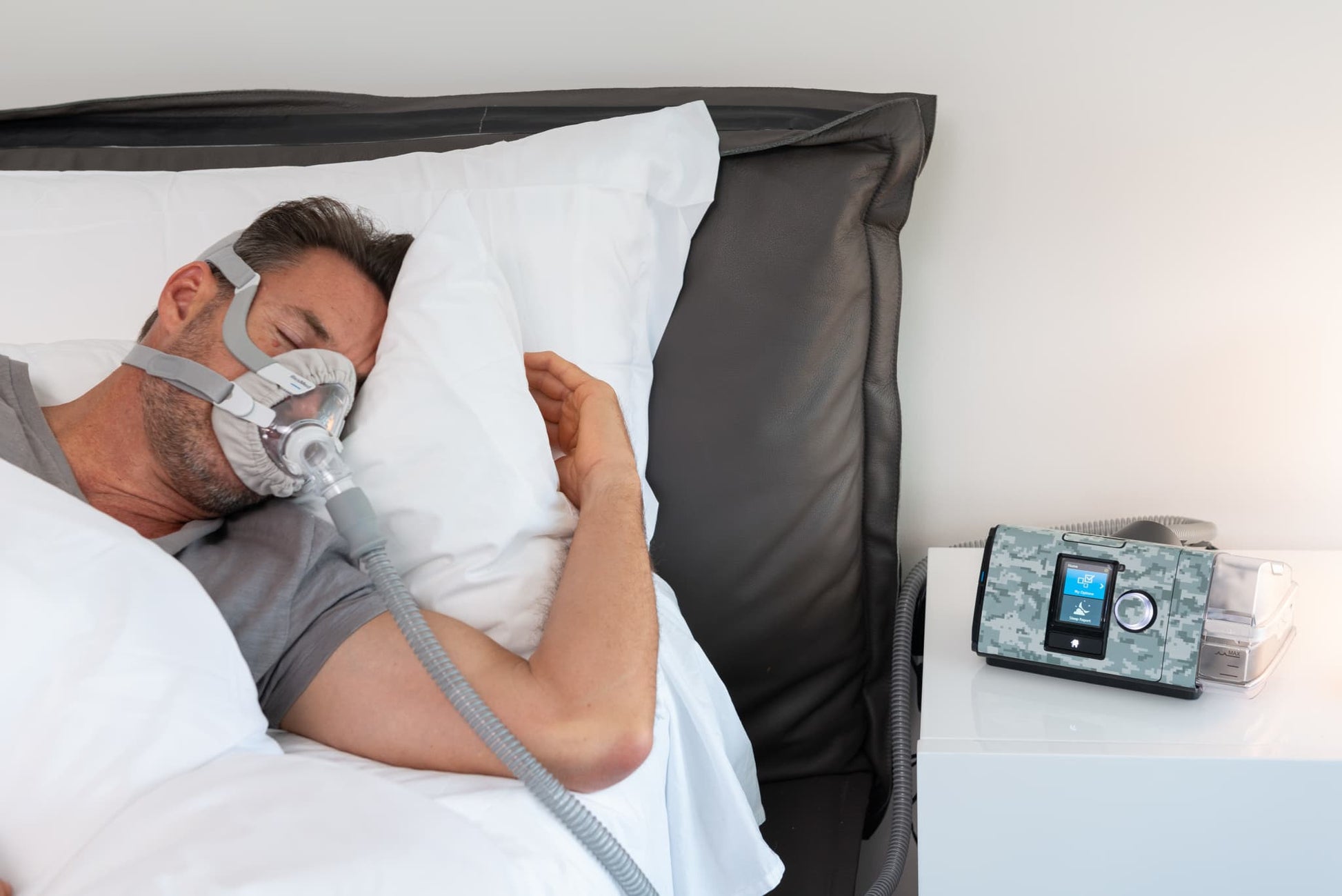 Man sleeping with a CPAP mask next to an AirSense 10 CPAP machine covered in a Snugell camouflage skin, adding a rugged look to the device.