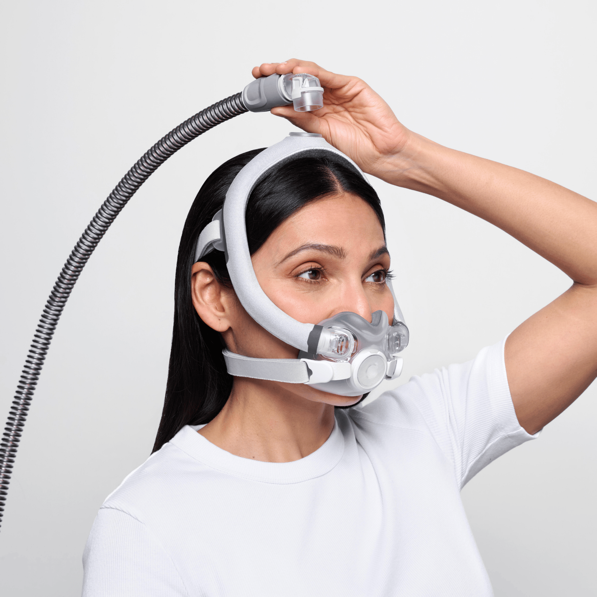 Woman wearing AirTouch F30i Comfort detaches hose from top of head using quick-release elbow.