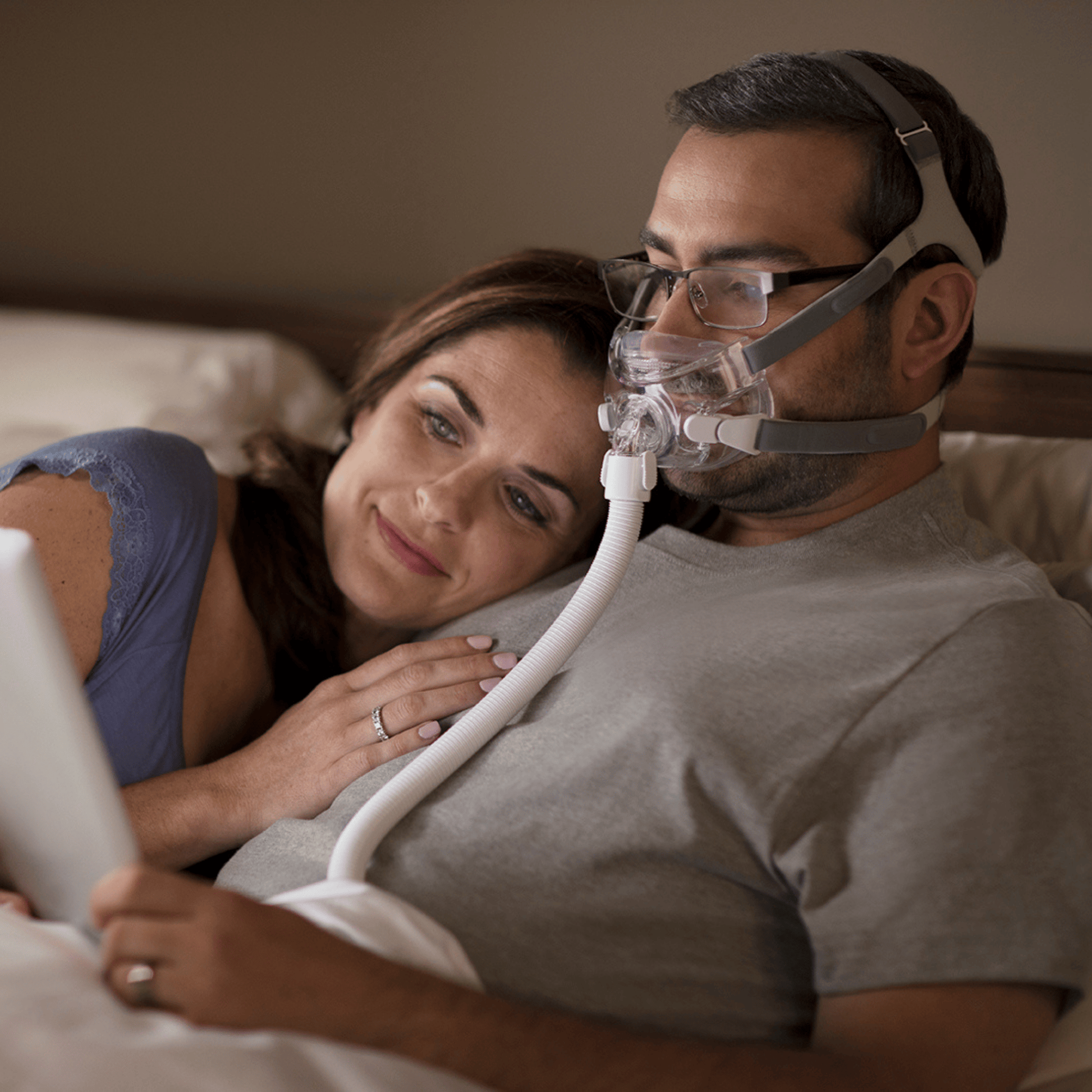 man wears amara view mask in bed while watching a movie on a tablet with his wife