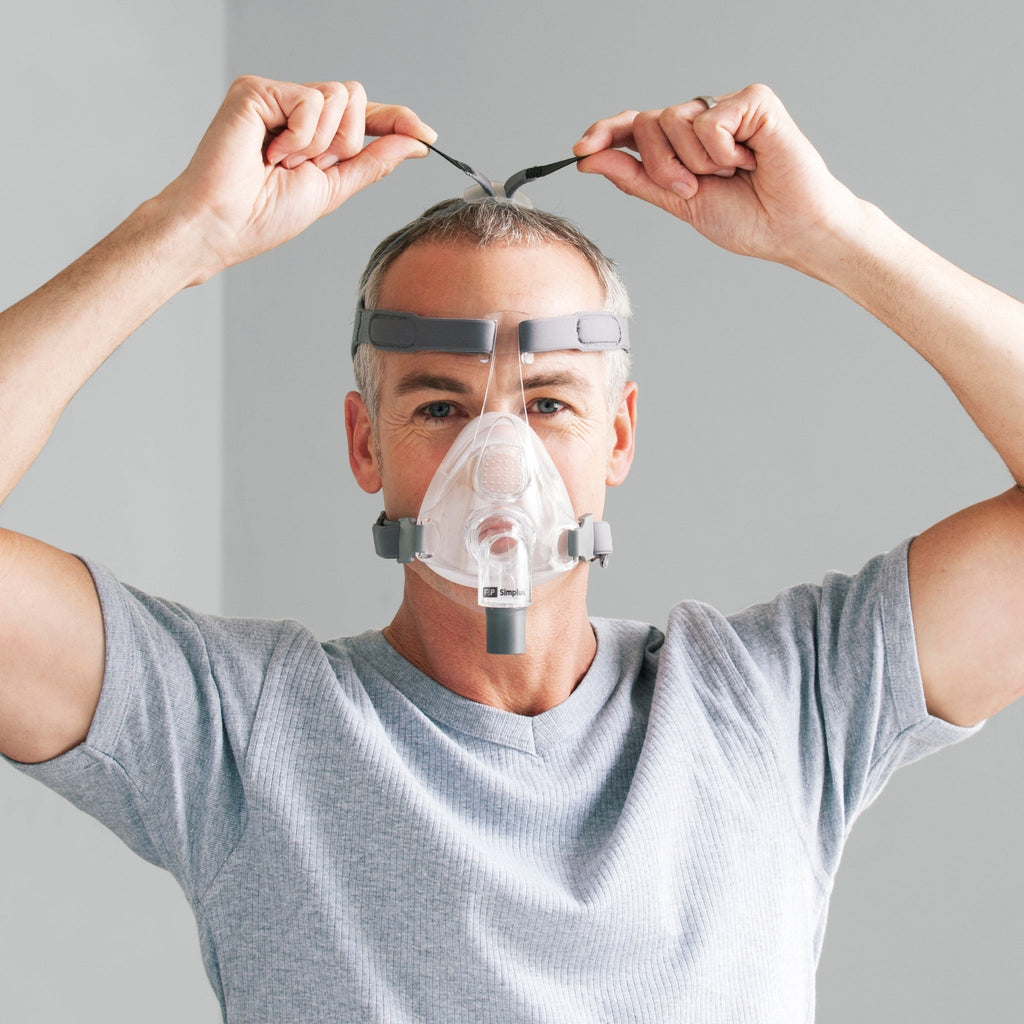 man wearing F&P simplus mask reaches up over his head to show off the dual crown strap adjustment points