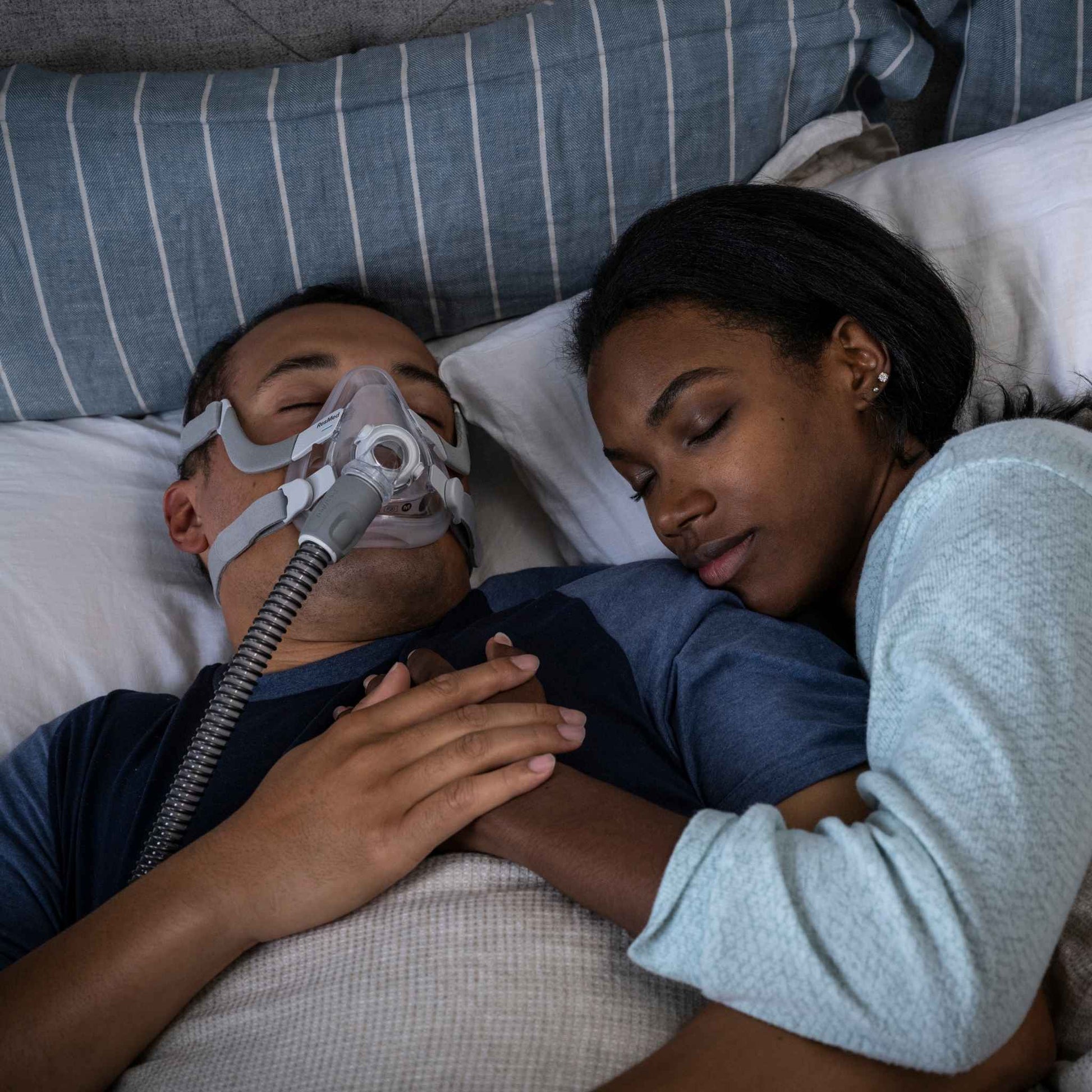 Man wearing airfit f20 full face cpap mask sleeps soundly next to his partner while holding hands