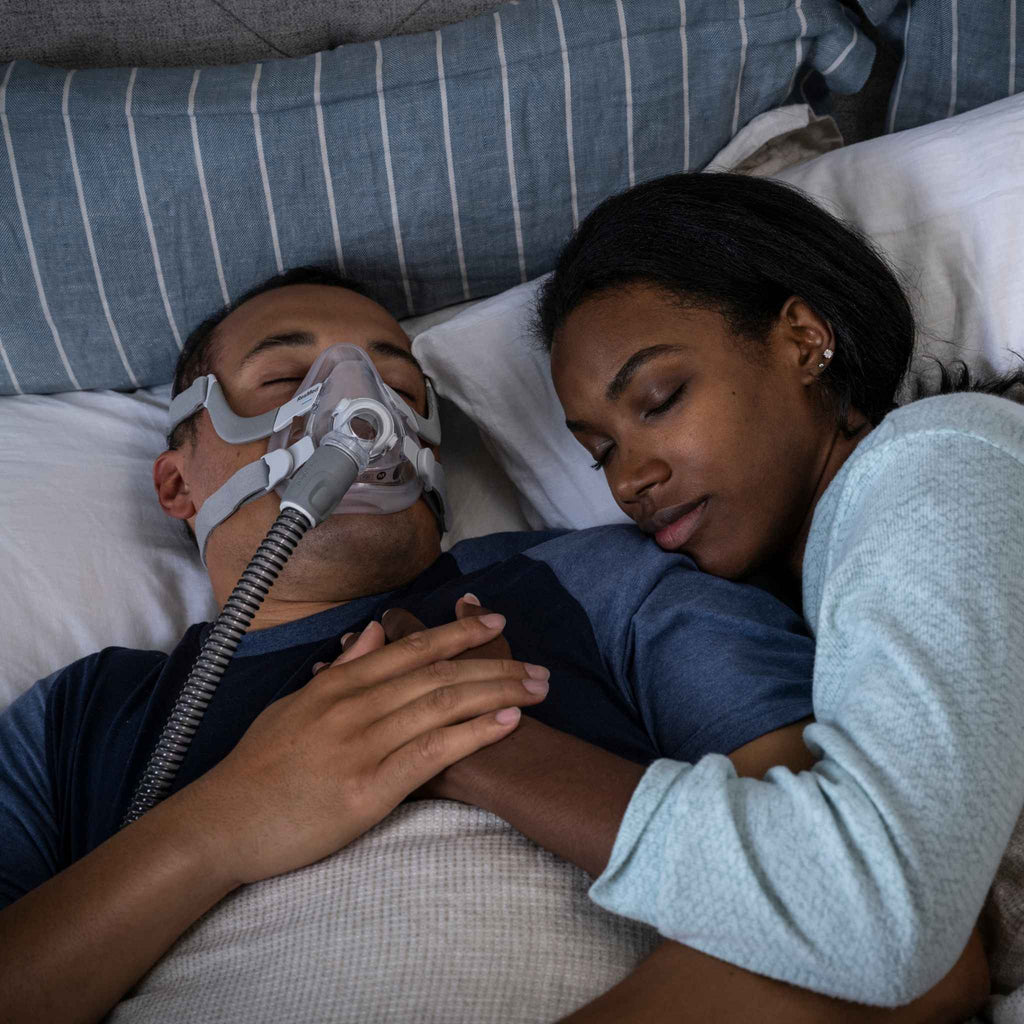Man wearing airfit f20 full face cpap mask sleeps soundly next to his partner while holding hands