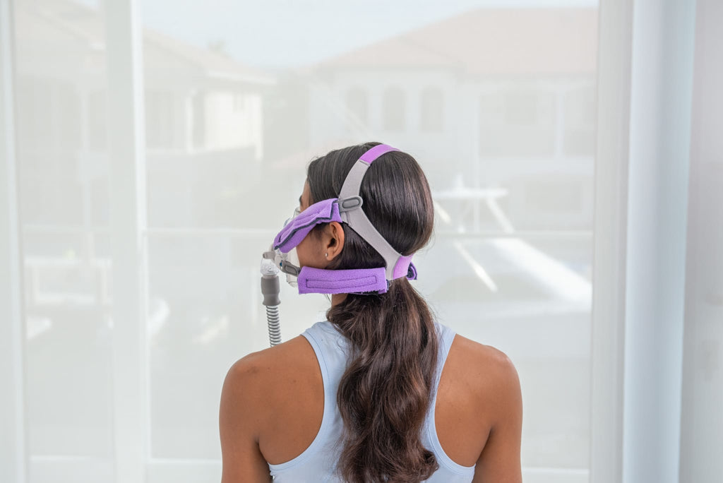 Woman wearing Snugell CPAP strap Cover in vibrant purple, providing soft cushioning for CPAP mask straps and reducing irritation.
