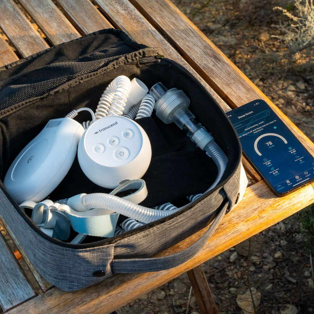 Bundle image showing the transcend micro, poweraway battery, airflex hose, airmist waterless humidifier, and a mask tucked into the sleepak travel bag. Sitting on a table next to a smartphone showing the dashboard of the mysleepdash therapy tracker app. 